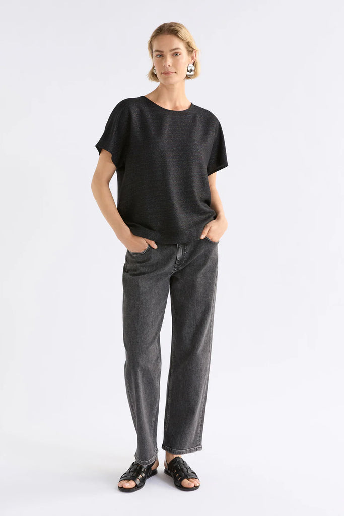 Woman wearing a black sparkly top and gray pants on a light gray background