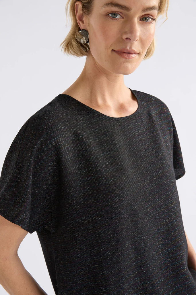 Woman wearing a black sparkly top on a light grey background