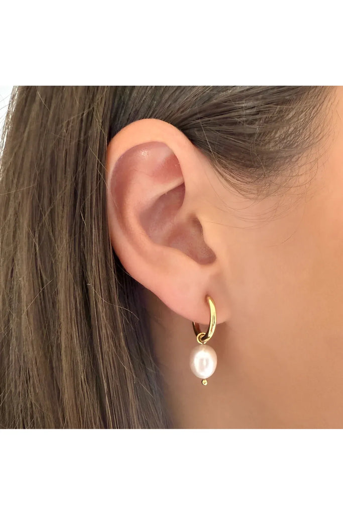 Gold hoop earring with a pearl pendant worn by a person. After Dark Pearl Hoop Earrings in gold by Ever.