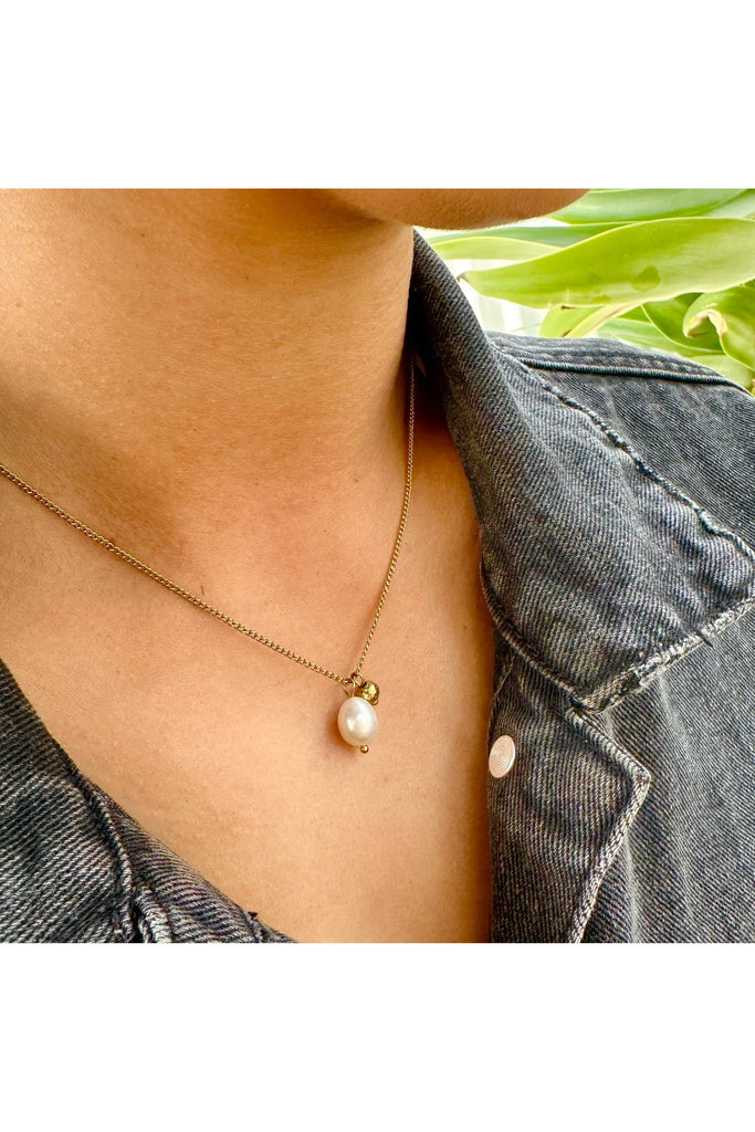Pearl necklace worn by a person with a denim jacket and green plant in the background. Ever Uptown Pearl Necklace.