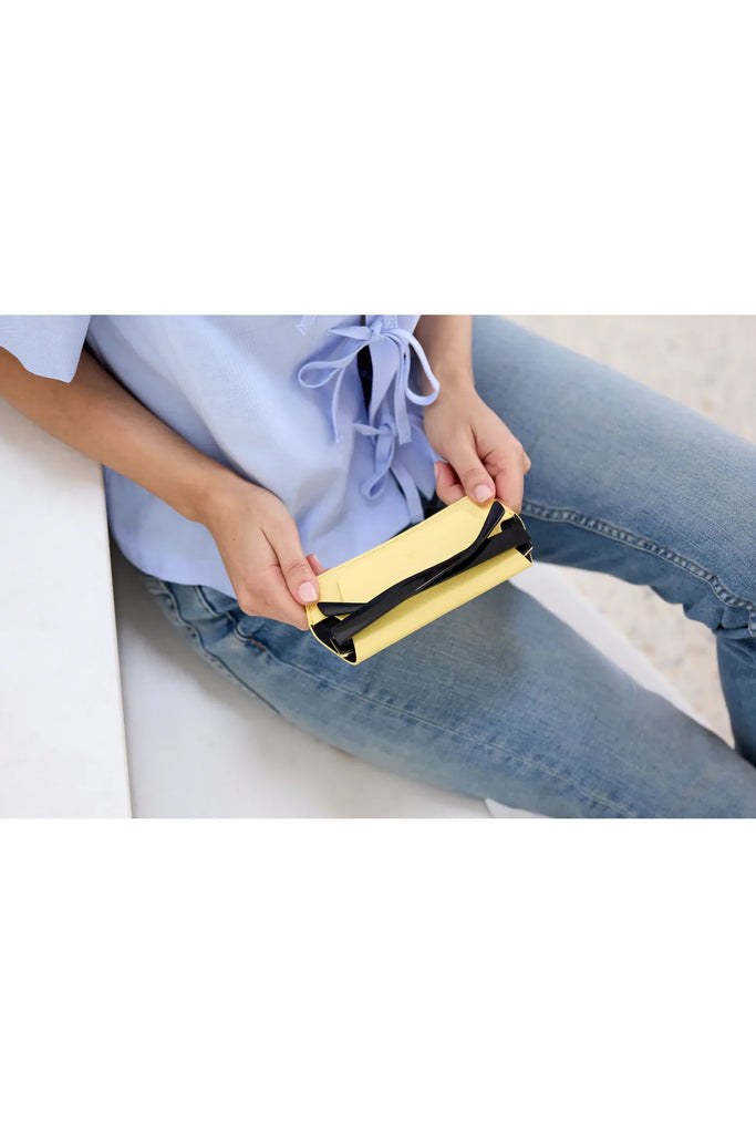 Person holding a yellow glasses case on a white surface