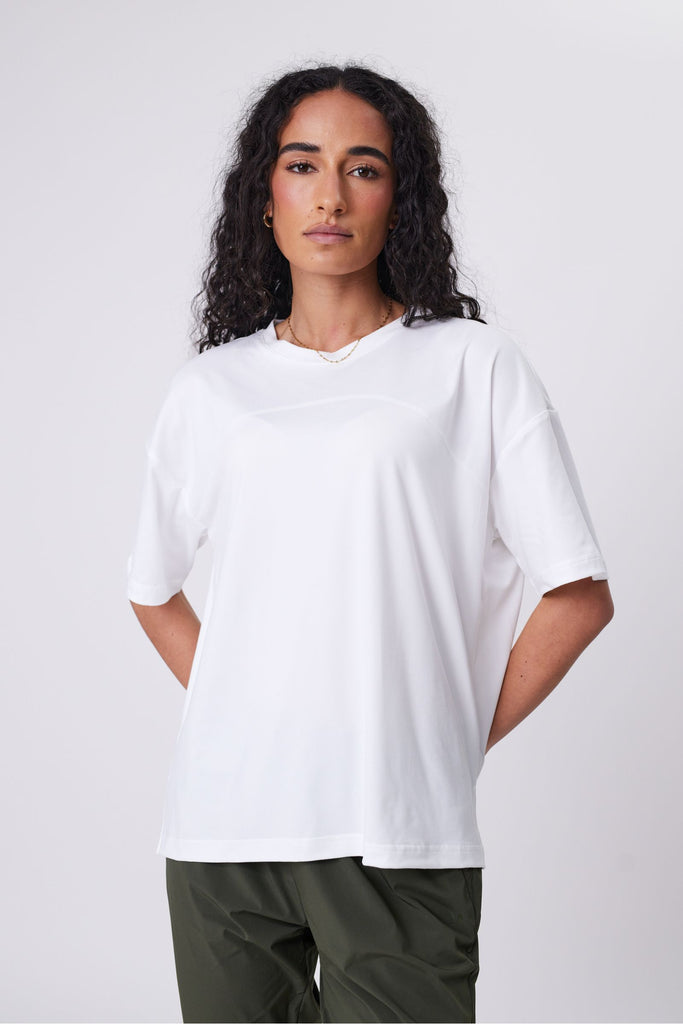 Woman wearing a white t-shirt and green pants on a plain background. Marlow Half time tee in Ivory short sleeve.