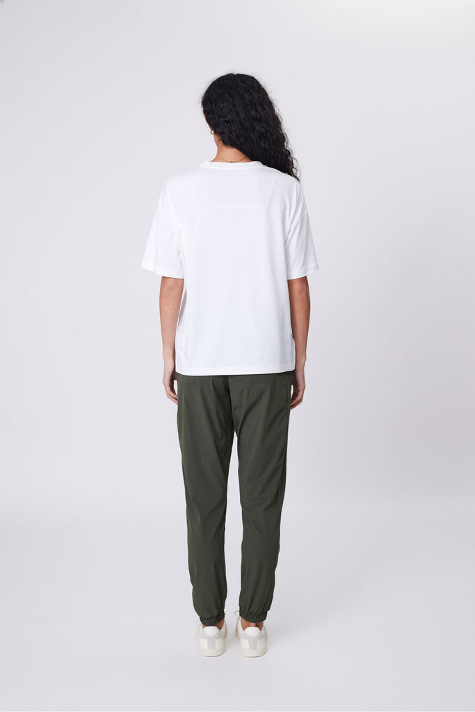 Woman wearing a white t-shirt and green pants on a plain background. Marlow Half time tee in Ivory short sleeve.