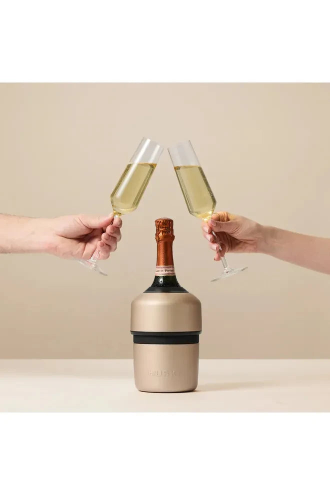 Huski Champagne Cooler in the Champagne Colourway standing with a bottle of Prosecco in it, while two hands are holding full glasses of Prosecco toasting each other above the Cooler