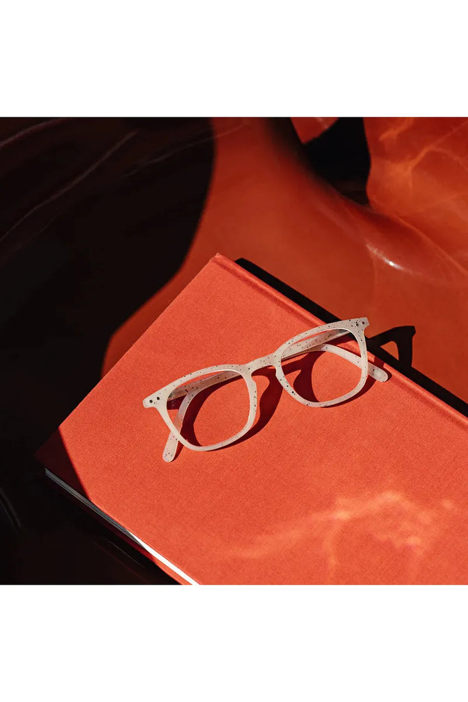 Izipizi Reading Glasses Artefact Collection Ceramic Beige Rectangular Frame Shape E Front View Lying on top of Red Woven Book Cover
