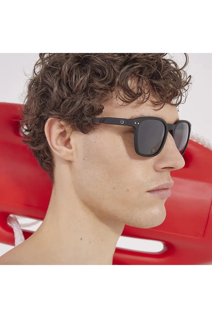 A man wearing black Izipizi polarised sunglasses with a red vehicle in the background.