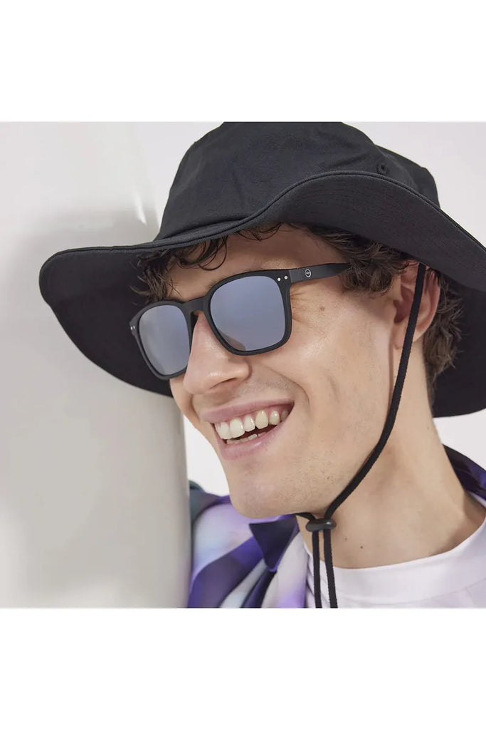 A man wearing a black bucket hat and black Izipizi polarised sunglasses against a white background.