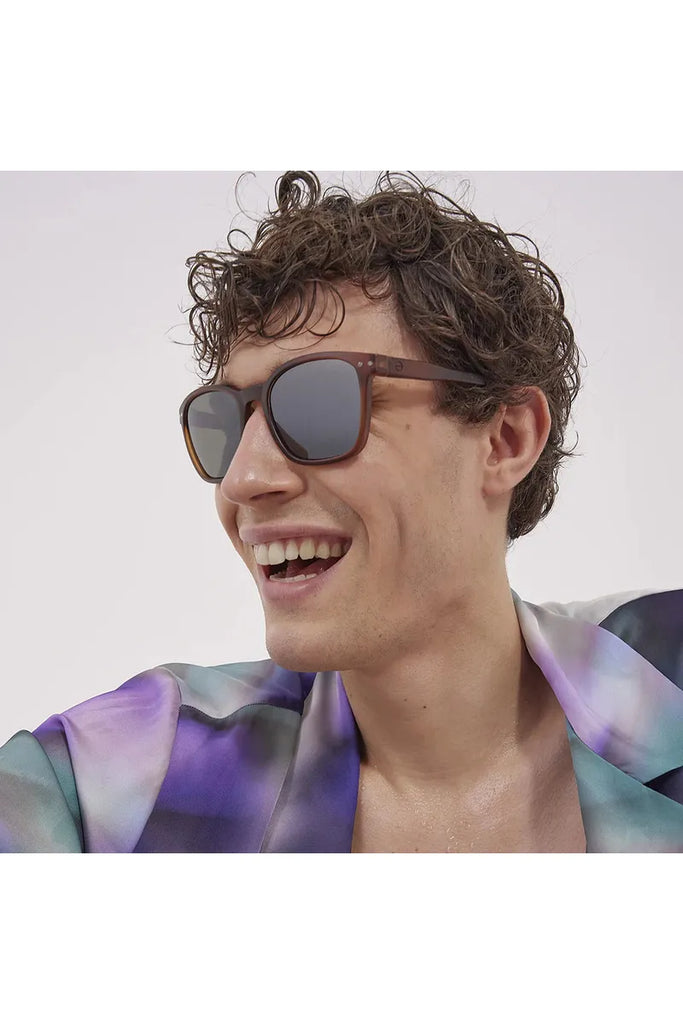 A man wearing Izipizi polarised sunglasses in Hazel Brown with a colourful shirt against a plain background.