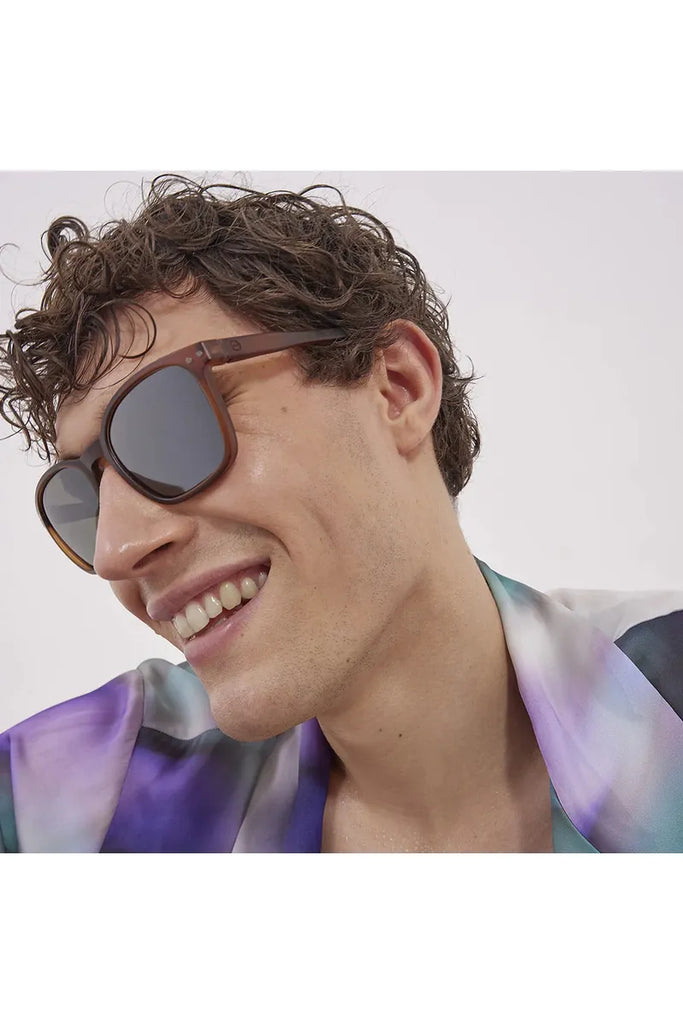 A man wearing Izipizi polarised hazel-brown sunglasses and a colourful shirt against a plain background.