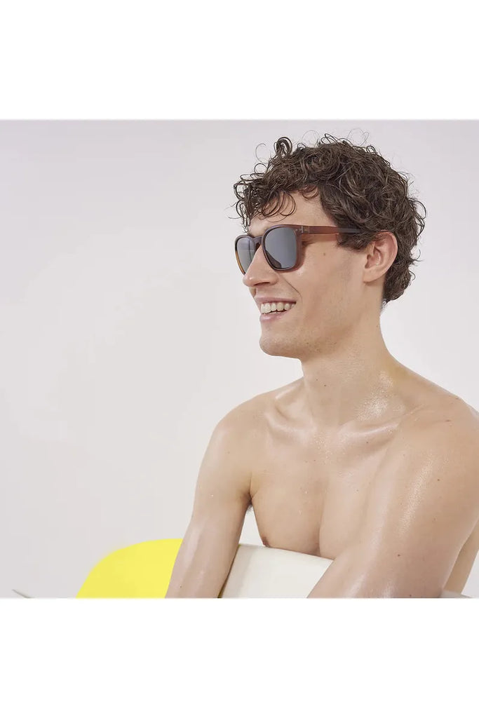 A man wearing Izipizi polarised sunglasses in hazel brown, with a yellow object in the background.