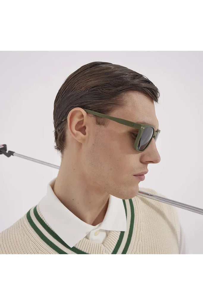 Man wearing Izipizi khaki green polarised sunglasses and a beige sweater with green stripes on a white background