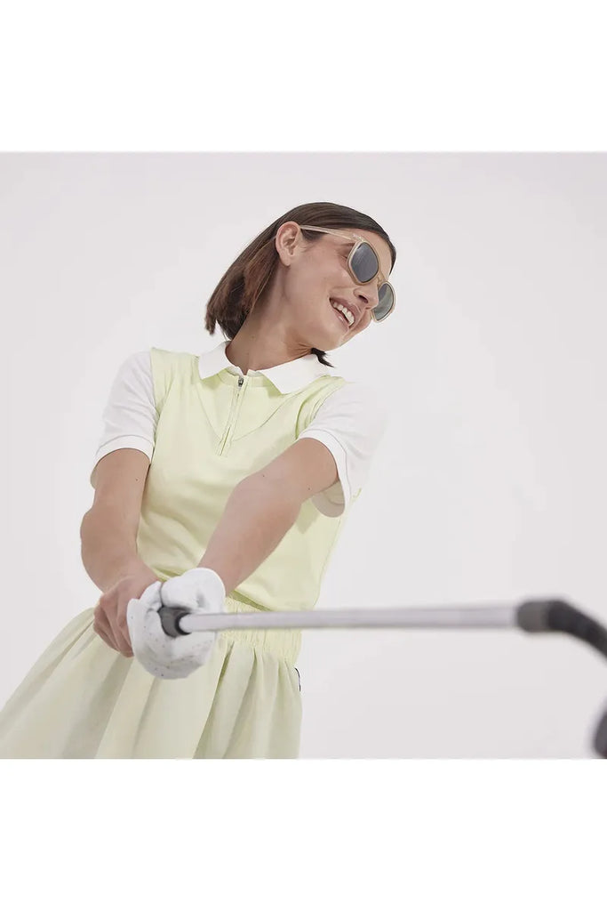 Woman in a yellow dress and izipizi Sports sunglasses holding a golf club against a white background