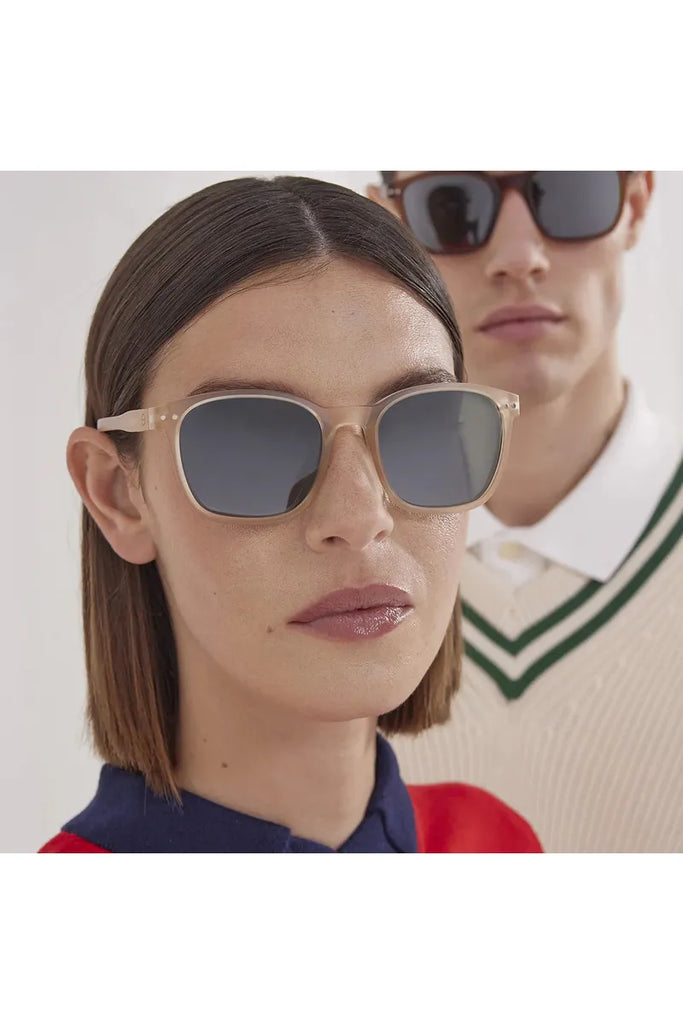 Close-up of a woman wearing beige izipizi sunglasses with a man in the background.