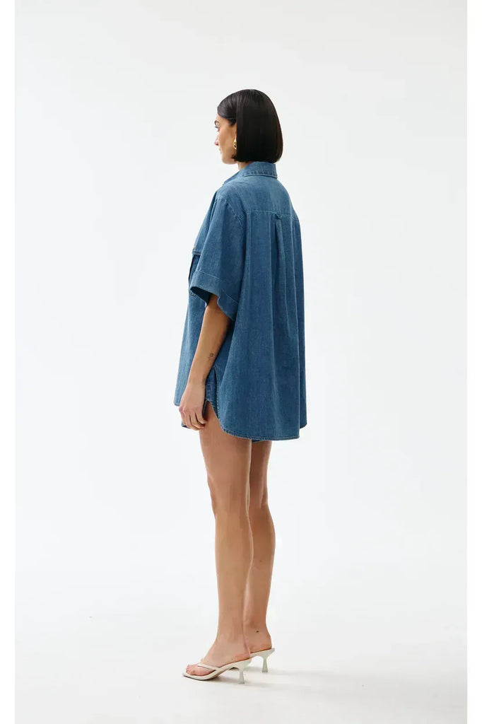 Woman wearing a blue denim outfit on a white background. Kinney Juniper Shorts with the matching Bella Shirt in a light denim fabric.