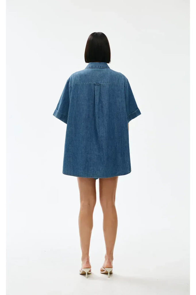 Woman wearing a blue denim outfit on a white background. Kinney Juniper Shorts with the matching Bella Shirt in a light denim fabric.