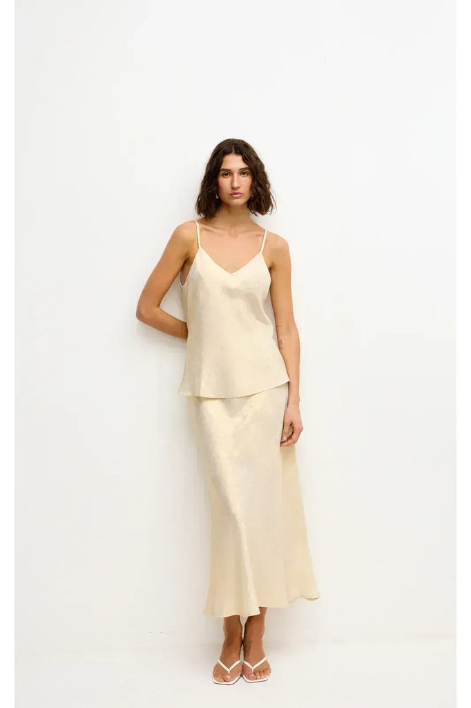 Woman wearing a gold top and long skirt on a white background. Kinney Gia Skirt in gold lurex.
