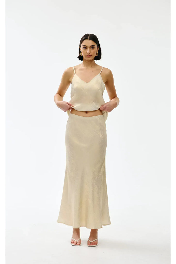 Woman wearing a gold top and long skirt on a white background. Kinney Gia Skirt in gold lurex.