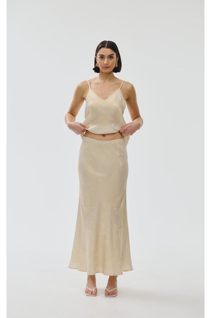 Woman wearing a gold top and long skirt on a white background. Kinney Gia Skirt in gold lurex.