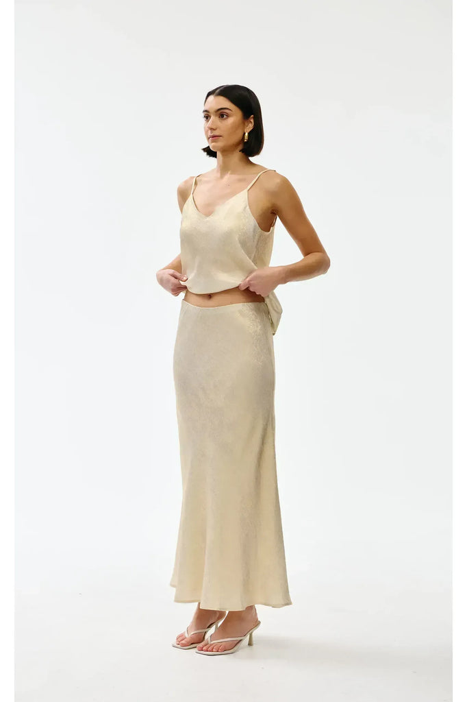 Woman wearing a gold top and long skirt on a white background. Kinney Gia Skirt in gold lurex.