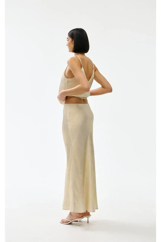 Woman wearing a gold top and long skirt on a white background. Kinney Gia Skirt in gold lurex.