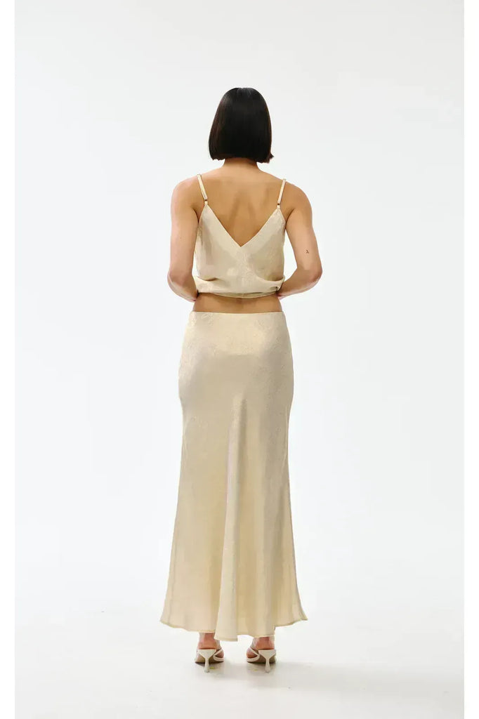 Woman wearing a gold top and long skirt on a white background. Kinney Gia Skirt in gold lurex.
