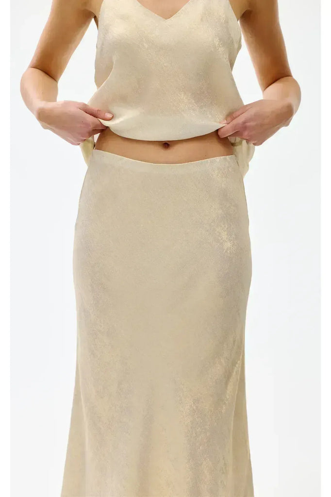 Woman wearing a gold top and long skirt on a white background. Kinney Gia Skirt in gold lurex.