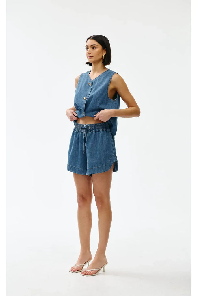 Woman wearing a blue denim outfit on a white background. Kinney Juniper Shorts.