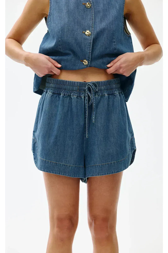 Woman wearing a blue denim outfit on a white background. Kinney Juniper Shorts in a light denim fabric.
