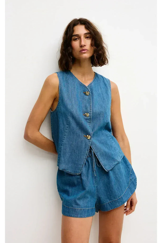 Woman wearing a blue denim outfit on a white background. Kinney Juniper Shorts in a light denim fabric.