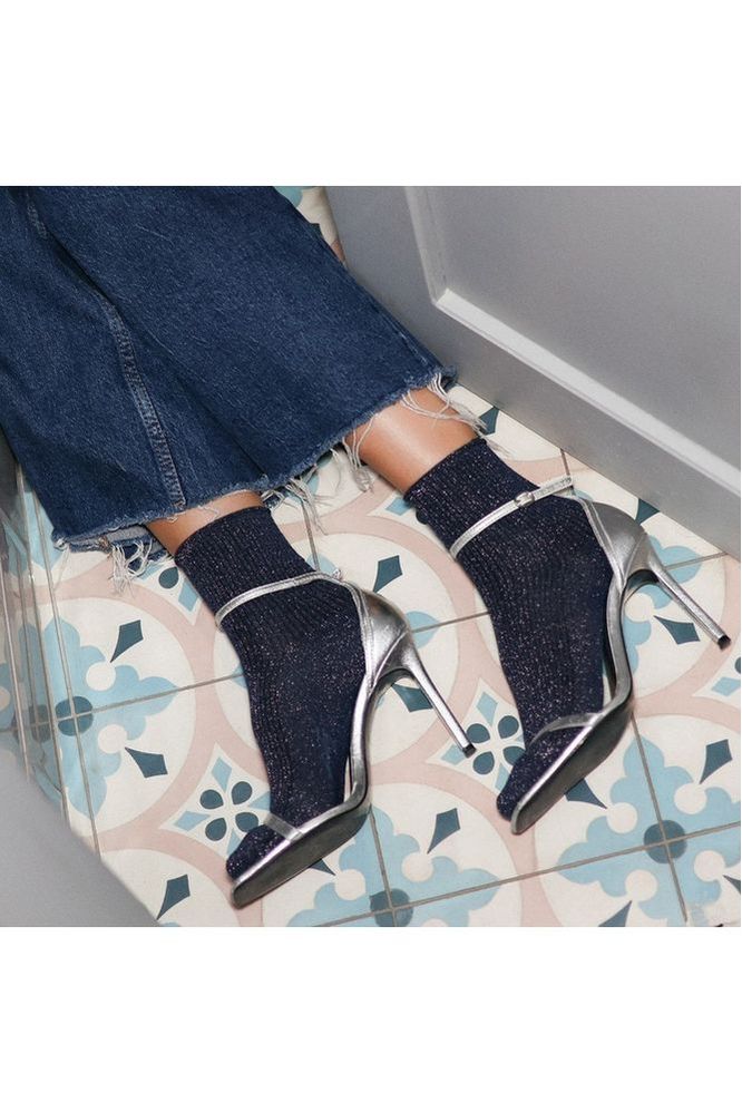 Person wearing Klue blue glittery socks with silver high-heeled shoes on a patterned floor.