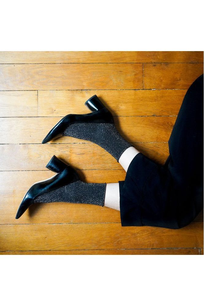 Person wearing black high-heeled shoes and black pants on a wooden floor with Klue Black Glitter socks