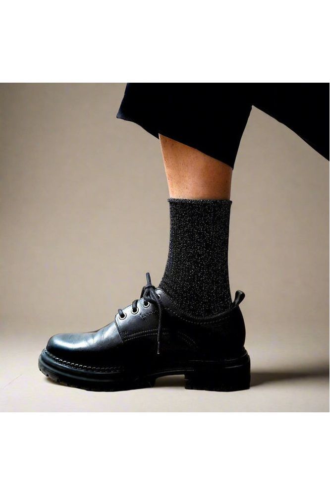 Person wearing black leather shoes and Klue Black Glitter socks on a neutral background