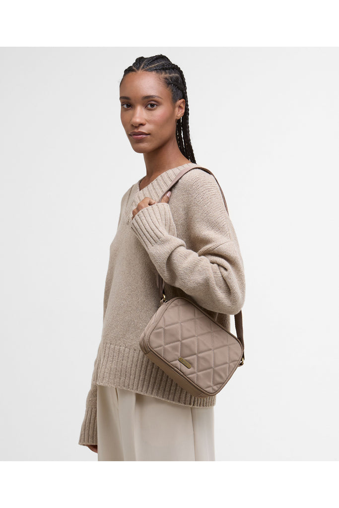 Quilted beige handbag on a light gray background. Barbour Quilted crossbody bag in sand.