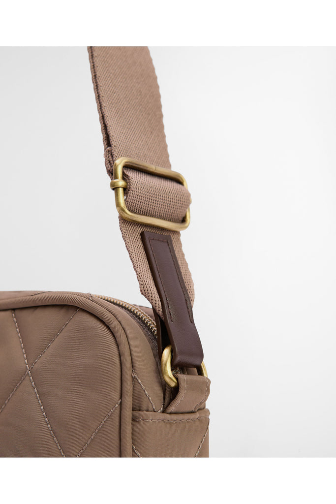 Quilted beige handbag on a light gray background. Barbour Quilted crossbody bag in sand.