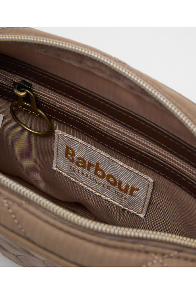 Quilted beige handbag on a light gray background. Barbour Quilted crossbody bag in sand.