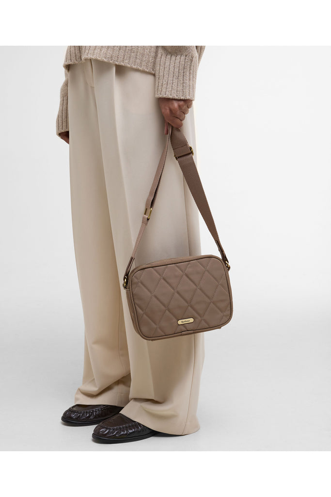 Quilted beige handbag on a light gray background. Barbour Quilted crossbody bag in sand.