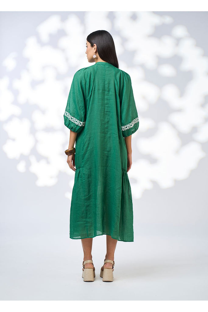 Woman wearing a green dress with white embroidery on a white background. Loobies Story Maya Midi dress in Palm Green.