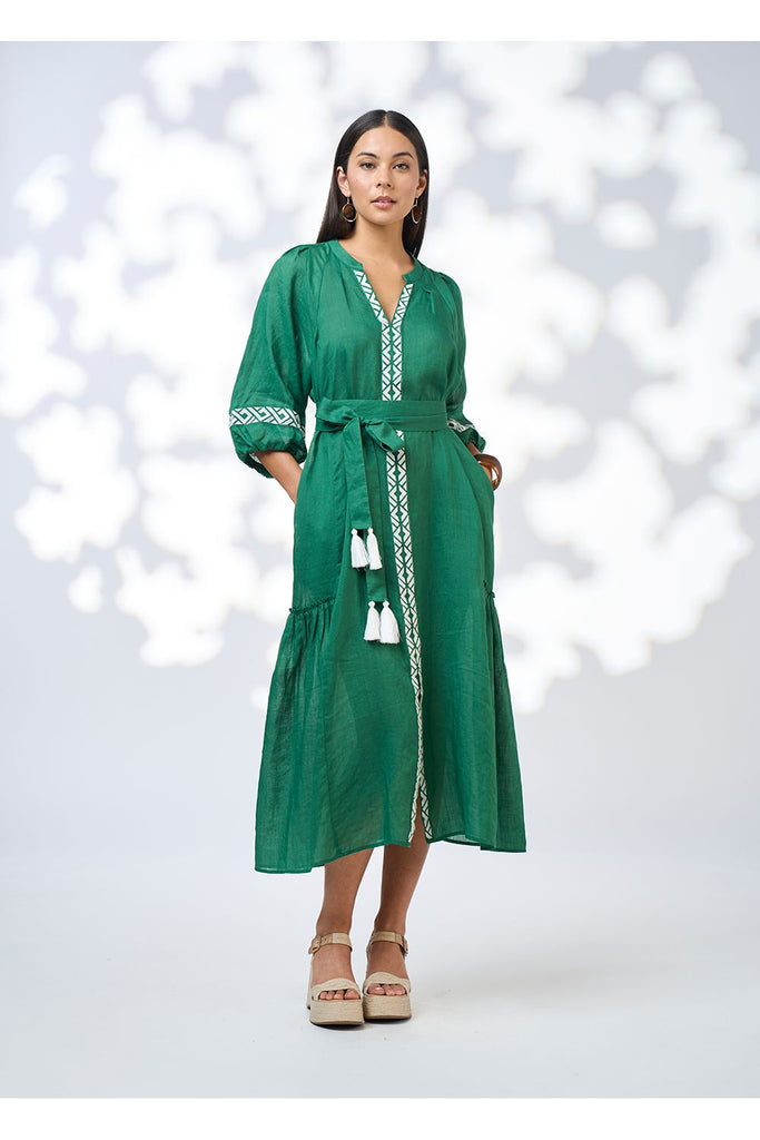 Woman wearing a green dress with white embroidery on a white background. Loobies Story Maya Midi dress in Palm Green.