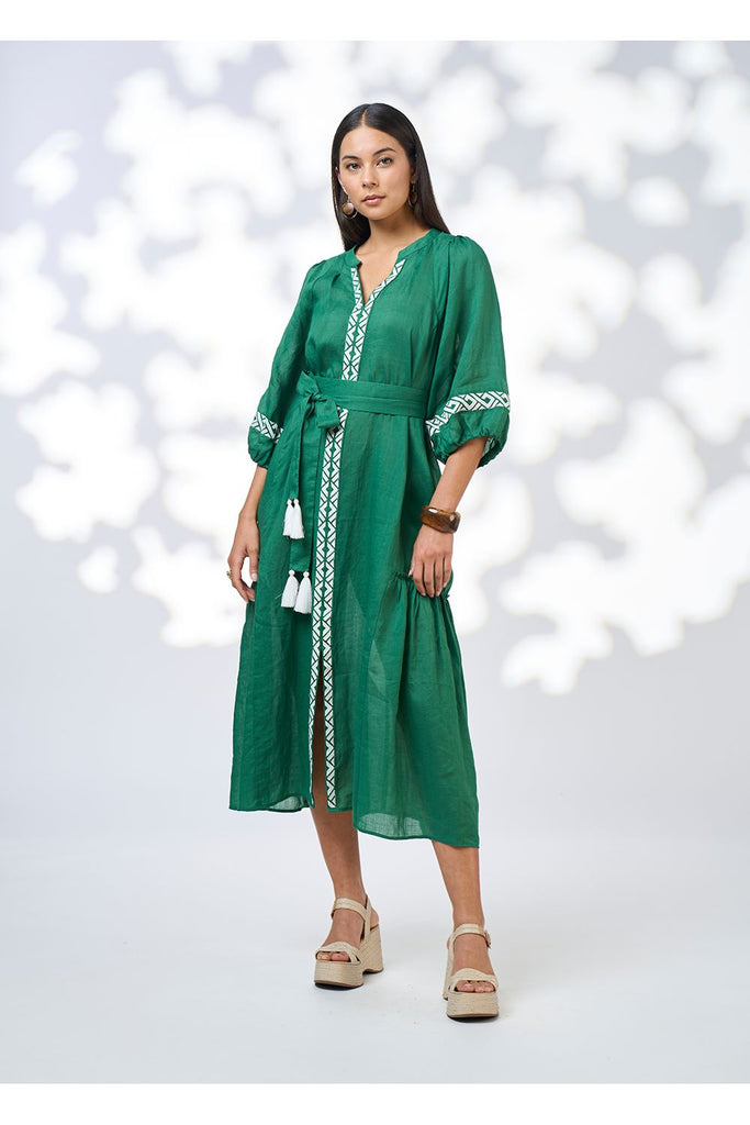 Woman wearing a green dress with white embroidery on a white background. Loobies Story Maya Midi dress in Palm Green.