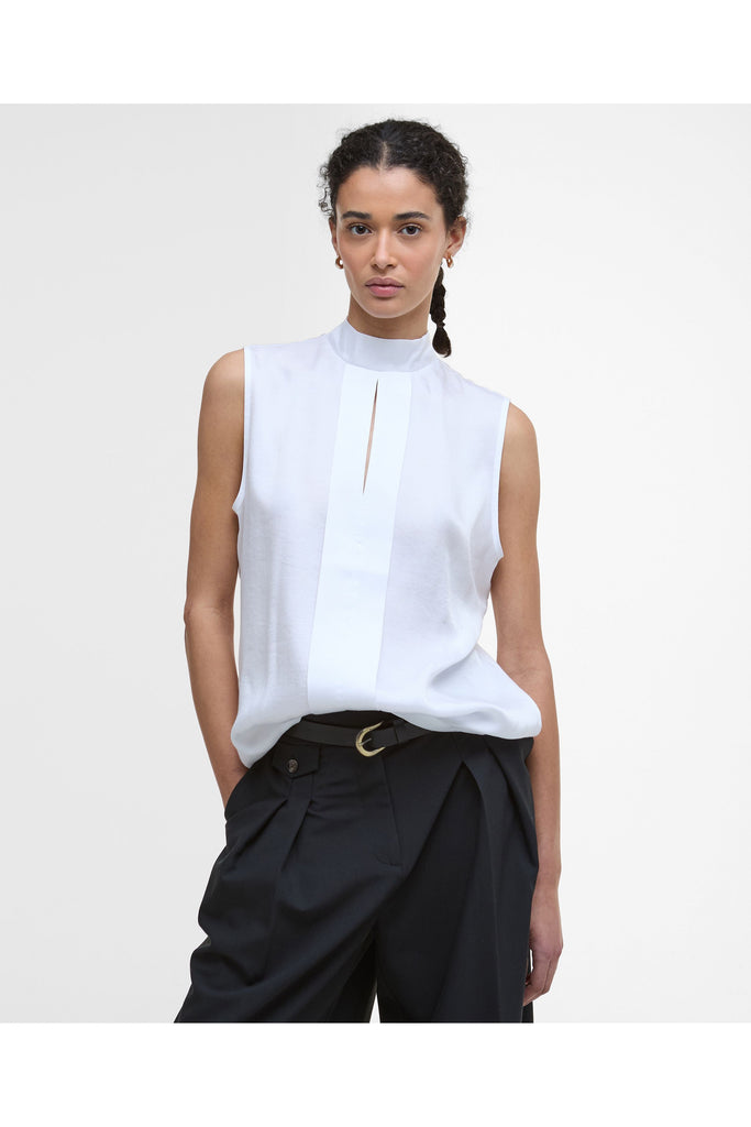 Woman wearing a white sleeveless top and black pants on a plain background. Barbour Sophia Top in White.