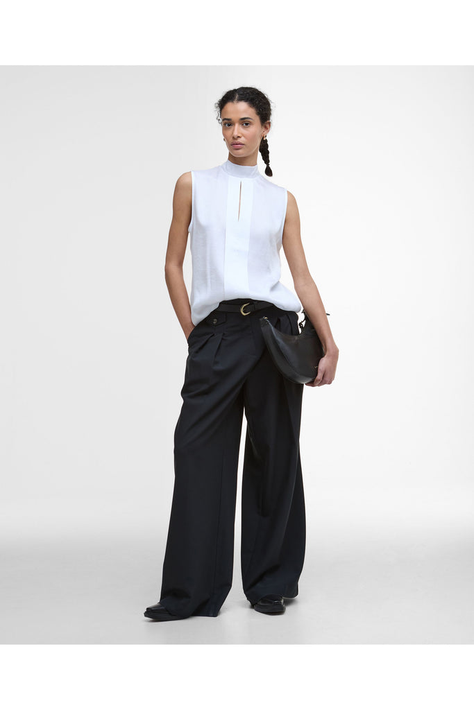 Woman wearing a white sleeveless top and black pants on a plain background. Barbour Sophia Top in White.