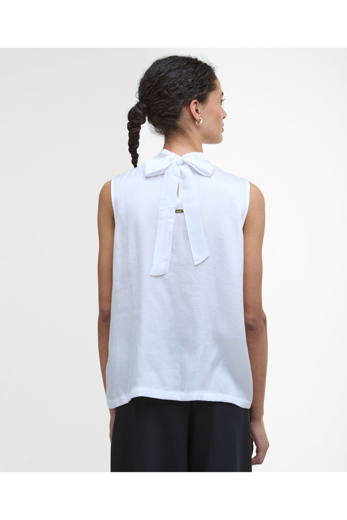 Woman wearing a white sleeveless top and black pants on a plain background. Barbour Sophia Top in White.