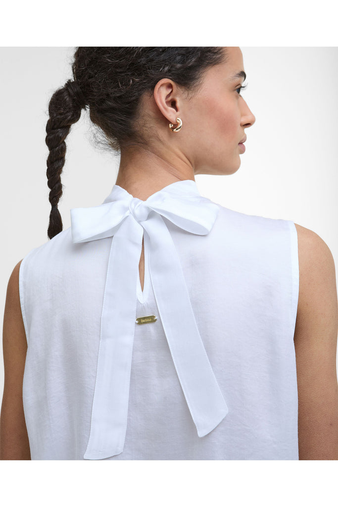 Woman wearing a white sleeveless top and black pants on a plain background. Barbour Sophia Top in White.