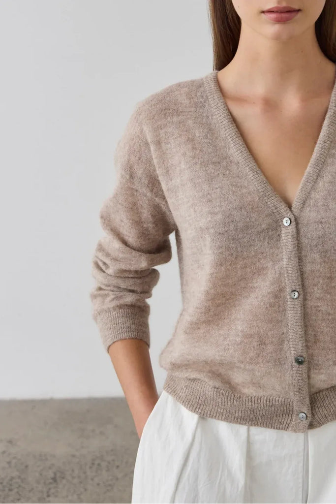 Woman wearing a beige cardigan over a white top. Laing Fine Alpaca Cardigan in Hazel.