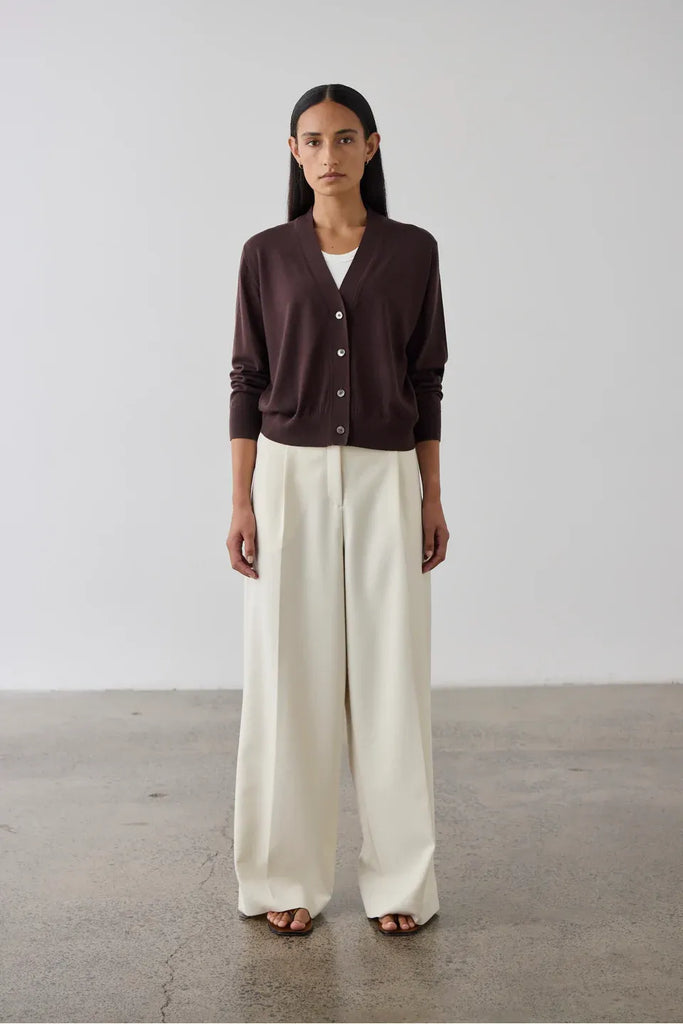 Woman wearing a dark bordeaux cardigan over a white top. Laing Merino V Neck Cardigan in Dark Bordeaux.