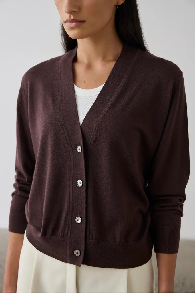 Woman wearing a dark bordeaux cardigan over a white top. Laing Merino V Neck Cardigan in Dark Bordeaux.