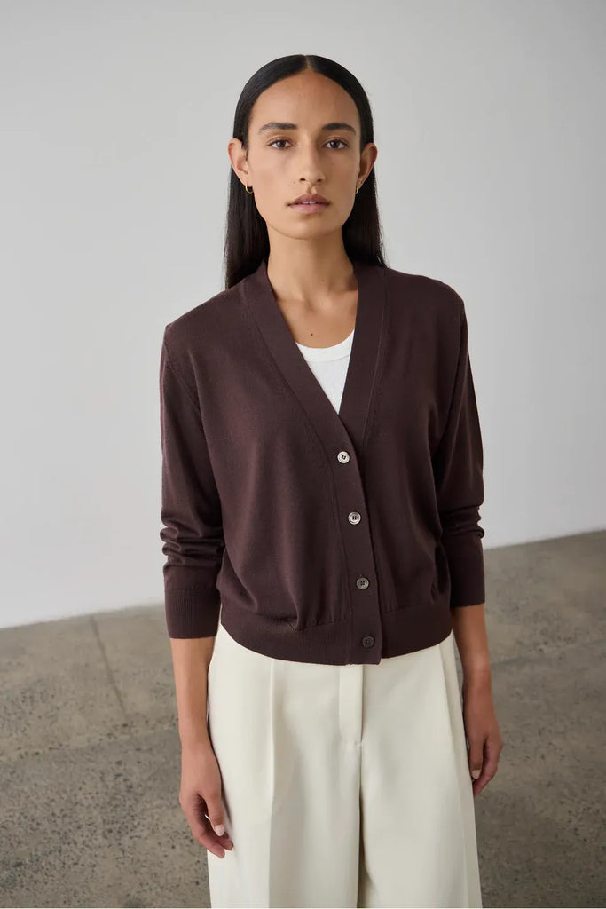 Woman wearing a dark bordeaux cardigan over a white top. Laing Merino V Neck Cardigan in Dark Bordeaux.