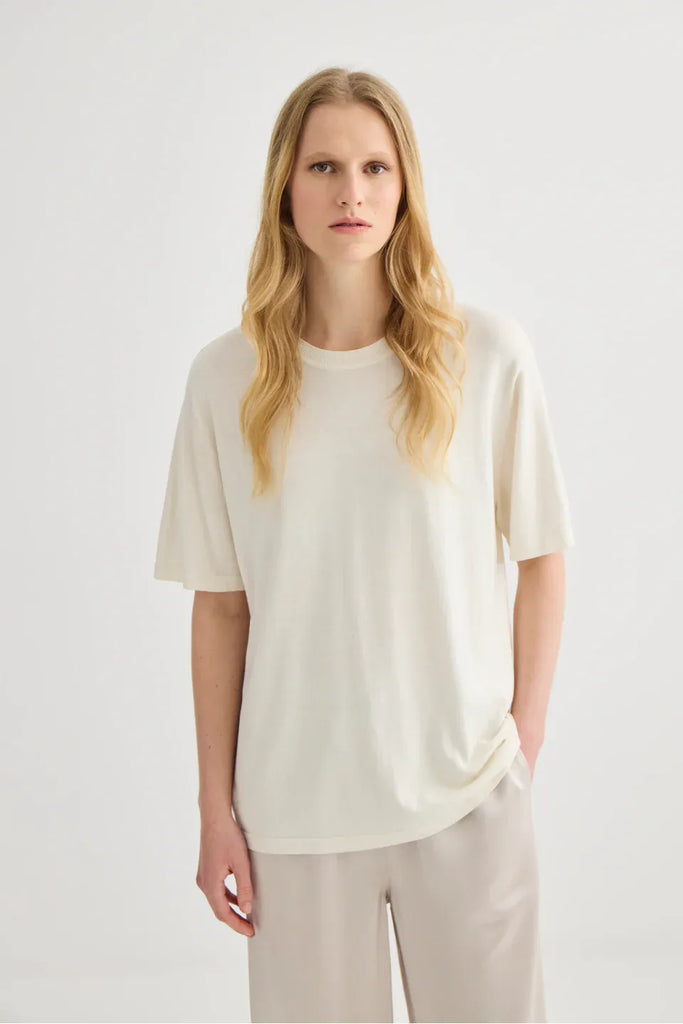 Woman wearing a white top and beige pants. Short Sleeve Silk Blend Knit Tee in Cream. 