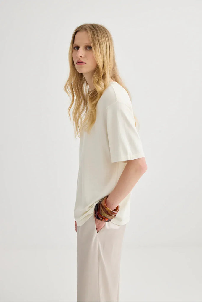 Woman wearing a white top and beige pants. Short Sleeve Silk Blend Knit Tee in Cream. 