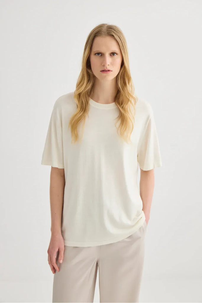 Woman wearing a white top and beige pants. Short Sleeve Silk Blend Knit Tee in Cream. 